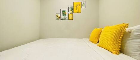 A bedroom with a bed, white bedding, and a yellow pillow.