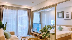 Et moderne hotelværelse med en stor seng, en sofa, et spisebord med et vinglas og et fjernsyn på et stativ.