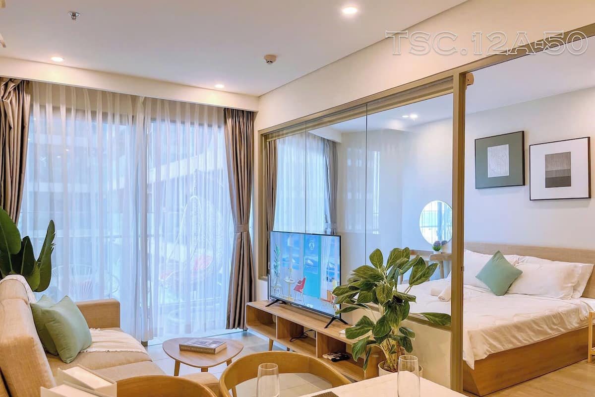 A modern hotel room with a large bed, a sofa, a dining table with a wine glass, and a TV on a stand.