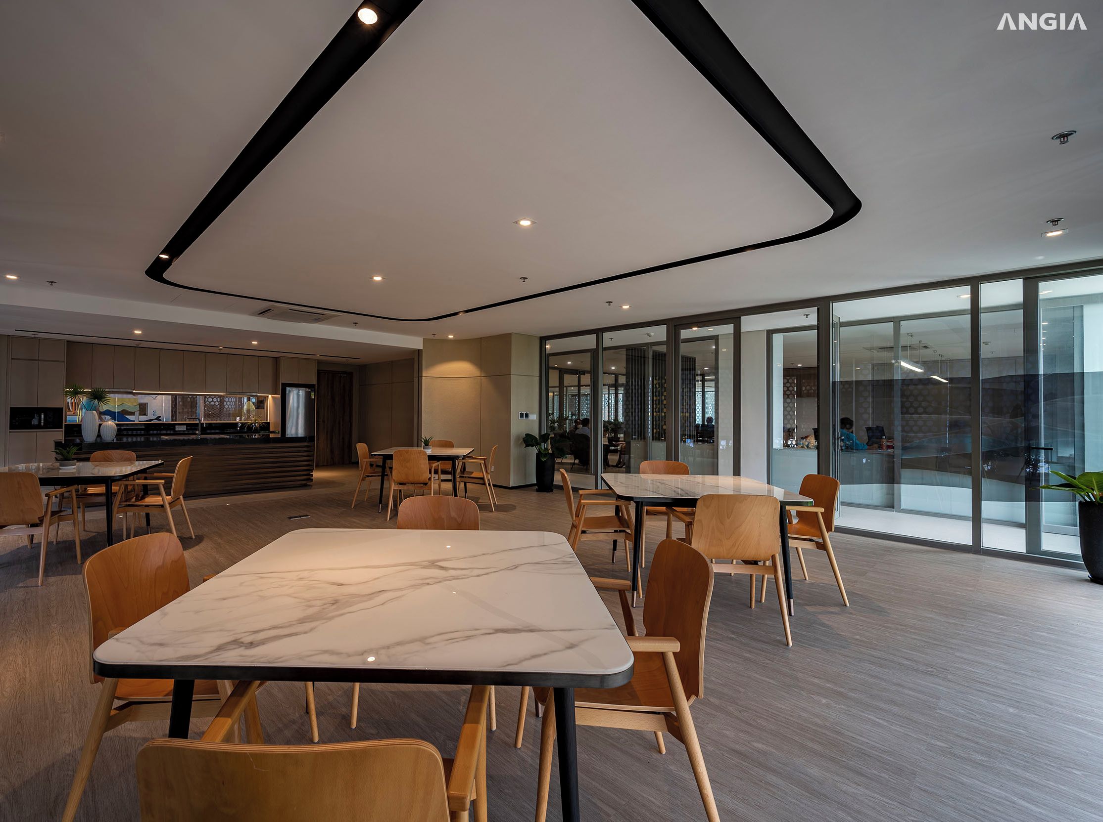 A modern dining area with marble tables and wooden chairs, large windows, and a kitchen in the background.