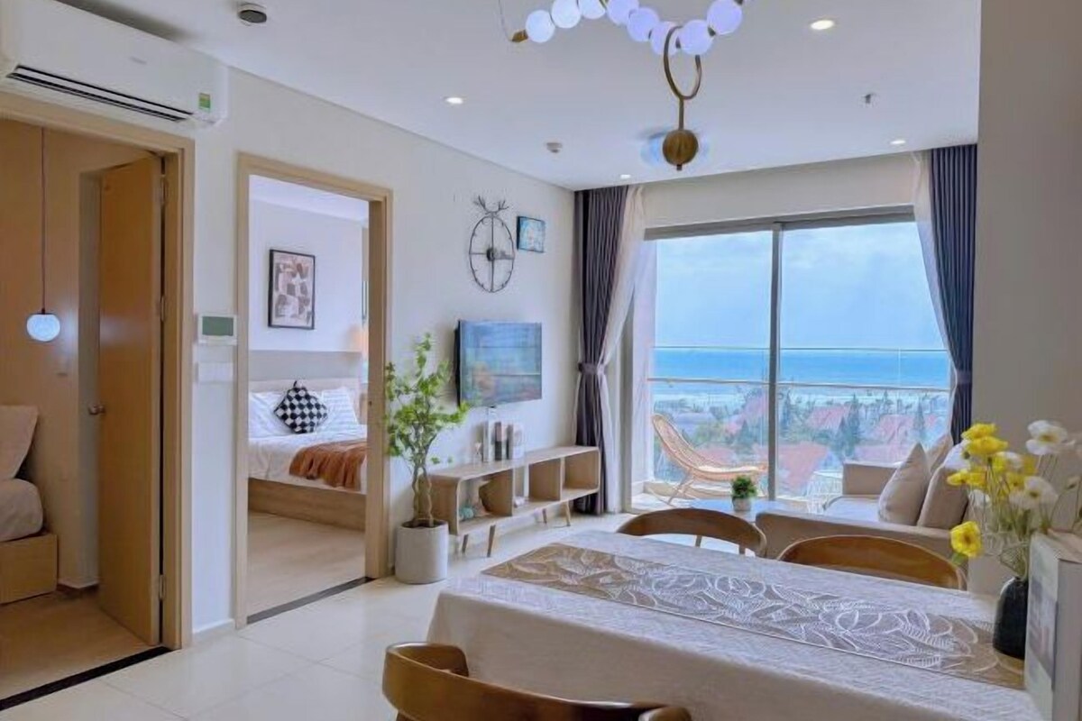 A modern hotel room with a balcony, a bed, a dining area, and a TV.