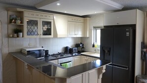 A modern kitchen with a large island, white cabinetry, and a black refrigerator. - Sunsets at Glenelg - entire 3 bedroom apartment
 (Glenelg)