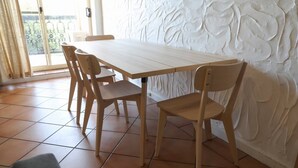 A dining area with a wooden table and chairs, a tiled floor, and a textured wall. - Sunsets at Glenelg - entire 3 bedroom apartment
 (Glenelg)