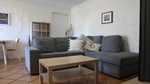 A living room with a grey sofa, a wooden coffee table, and a white textured wall. - Sunsets at Glenelg - entire 3 bedroom apartment
 (Glenelg)