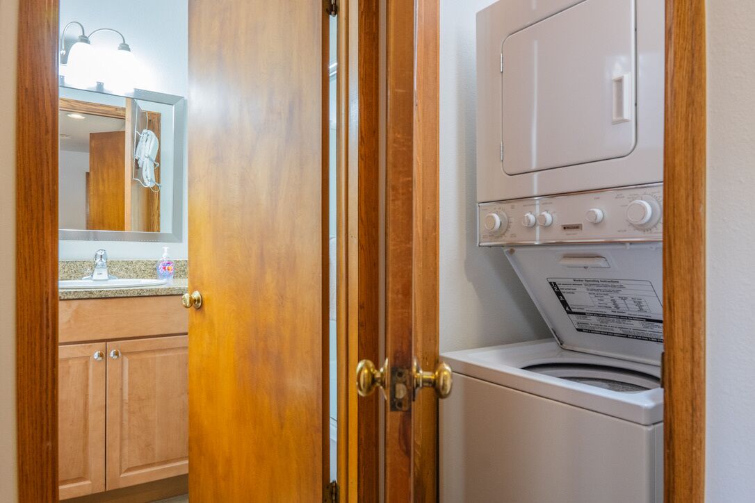 A laundry room with a washer and dryer, wooden cabinets, and a mirror with lights above the sink.