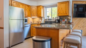 Een moderne keuken met houten kasten, een roestvrijstalen koelkast, een granieten aanrechtblad en een geïntegreerd eiland met barstoelen.