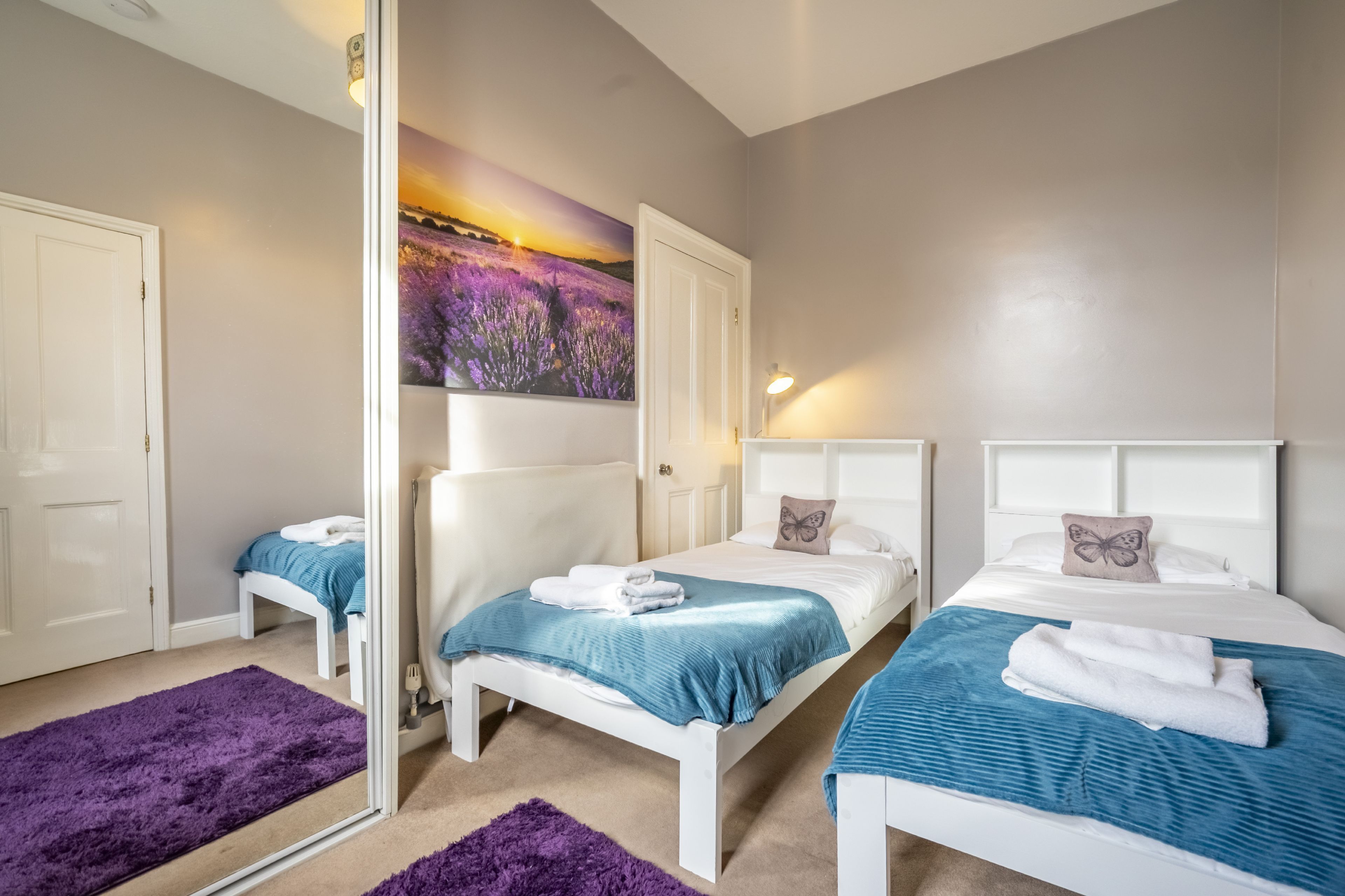 Un dormitorio con dos camas, un espejo grande y un cuadro de campos de lavanda.