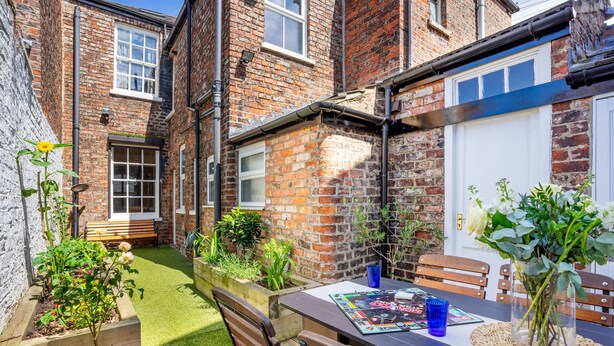 A brick house with a small garden, a wooden bench, and a table with a magazine and a vase of flowers. - Aycliffe Cottage  -  a family break that sleeps 6 guests  in 3 bedrooms (York)