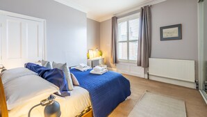 A bedroom with a bed, bedside table, lamp, and a window with curtains. - Aycliffe Cottage  -  a family break that sleeps 6 guests  in 3 bedrooms (York)