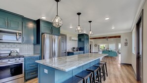 Una cocina moderna con gabinetes color aguamarina, electrodomésticos de acero inoxidable, una isla de mármol y taburetes de bar.