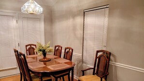 A dining room with a wooden table and chairs, a vase with flowers, and a chandelier. - Clean Comfy Cottage - Near Downtown High Point Furniture Market, Hospitals & HPU (High Point)