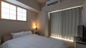 Habitación de hotel con una cama grande, una mesita de noche con lámpara, televisión y ventana con cortinas.