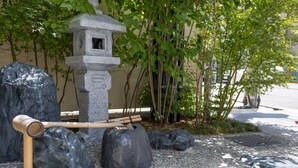 Un farol de piedra con rastrillo de bambú, rodeado de rocas grandes y follaje.