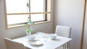 Una mesa de comedor blanca con cuatro cuencos, dos vasos y palillos. Hay una planta en maceta sobre la mesa.
