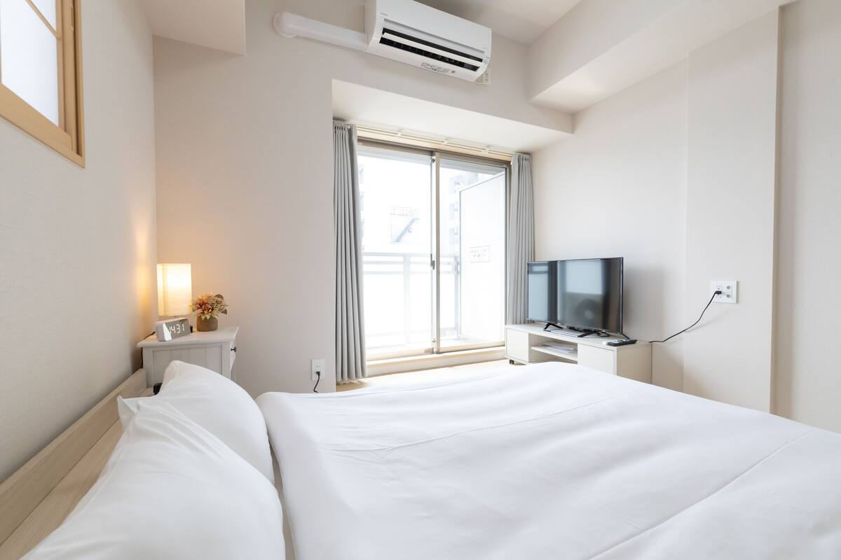 Quarto de hotel com cama, televisão, janela com cortinas e ar condicionado.