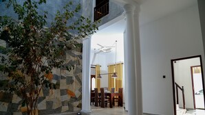 Un espacio interior amplio con una pared de piedra, una planta en maceta y una zona de comedor con sillas y una mesa.