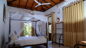 Un dormitorio con una cama con dosel, un ventilador de techo, una mesita de noche con lámpara y una ventana con cortinas.