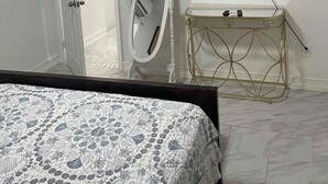 A bedroom with a bed, a TV mounted on the wall, a vanity table with a mirror, and a door leading to another room. - COMFORTABLE ORLANDO PRIVATE STUDIO W/FULL KITCHEN! (Orlando)