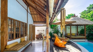 Eine Holzterrasse mit einer strohgedeckten Struktur, einem Pool und einer Sitzecke mit Kissen.