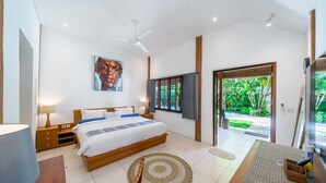 Ein modernes Hotelzimmer mit einem großen Bett, einem Deckenventilator, einem Gemälde an der Wand und Blick auf den Garten durch die Tür.