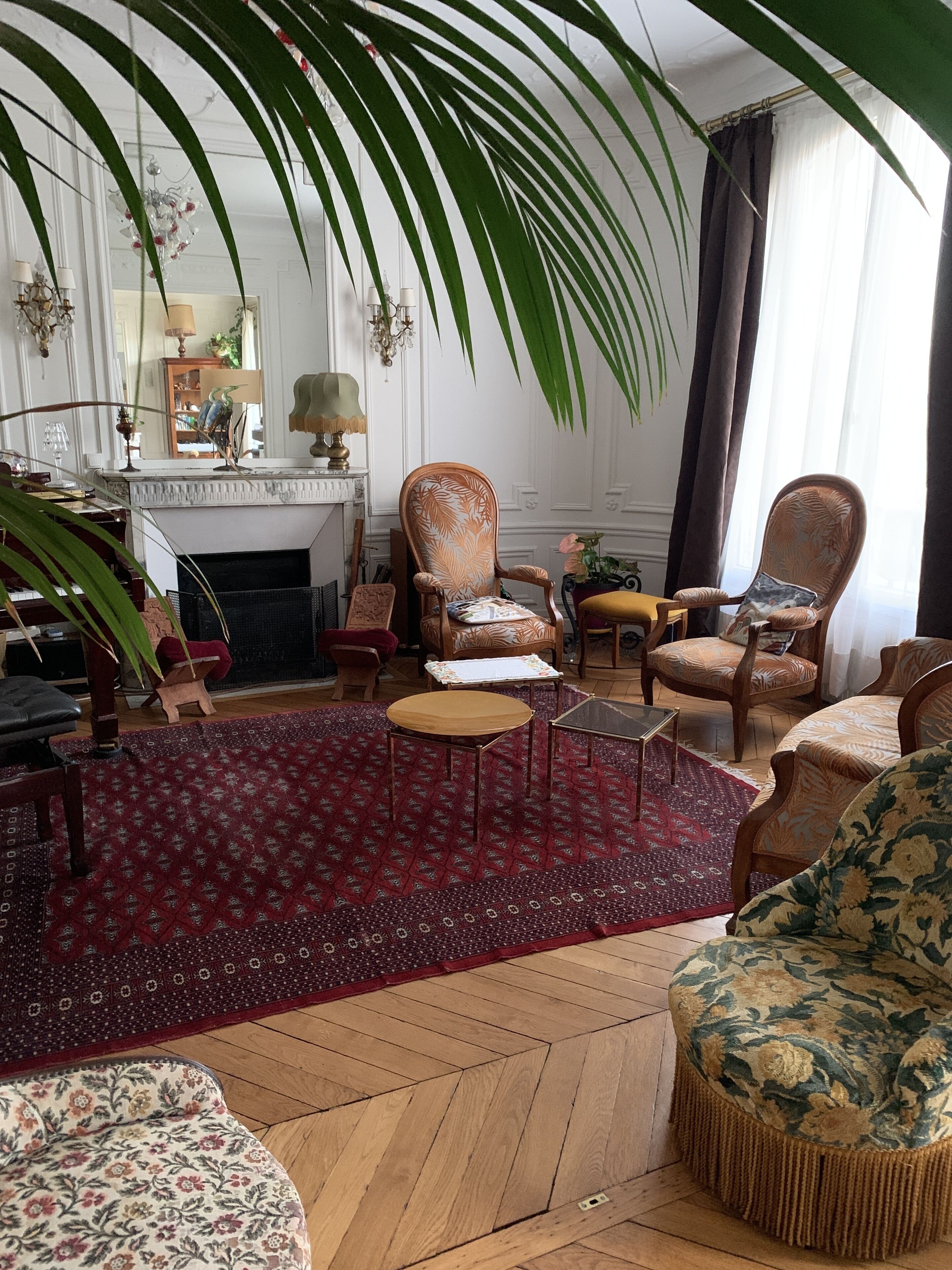 Un salón con chimenea, varias sillas, una mesa redonda y una alfombra grande con motivos rojos.