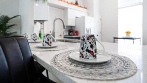 A modern kitchen with white cabinets, a central island with a round table, and a hanging plant.