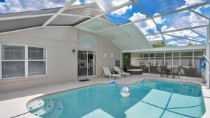 An indoor swimming pool with a glass ceiling, lounge chairs, and a patio area.