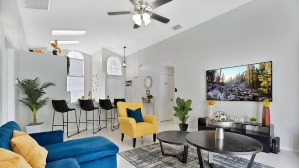A modern living room with a blue sofa, yellow armchair, and a dining table with chairs.