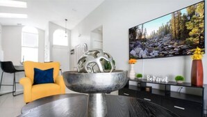 A modern living room with a dark wooden table, a yellow armchair, and a large flat-screen TV displaying a forest scene.