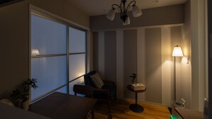 A room with a large window, a chair, a small table, a floor lamp, and a ceiling light fixture. - H2H Tsutenkaku (Osaka)