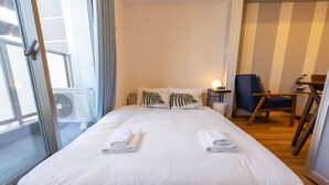 A hotel room with a large bed, two pillows, a bedside table with a lamp, a chair, and a view of the outside. - H2H Tsutenkaku (Osaka)
