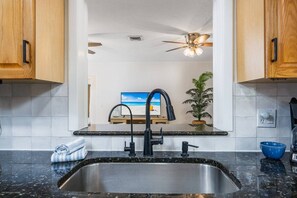 A kitchen with a stainless steel sink, wooden cabinets, a ceiling fan, and a potted plant. - Relax in Peace | Dog Friendly | 1 mile to Beach (Nokomis)