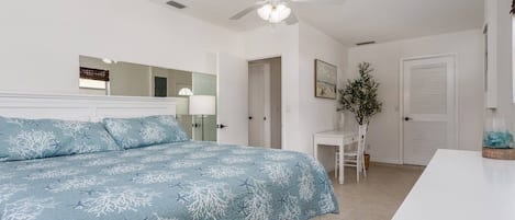 Quarto com cama, ventilador de teto, mesa de cabeceira branca e porta.