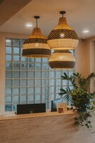 Zona de recepción con mostrador de madera, dos lámparas colgantes de mimbre, una computadora y una planta.