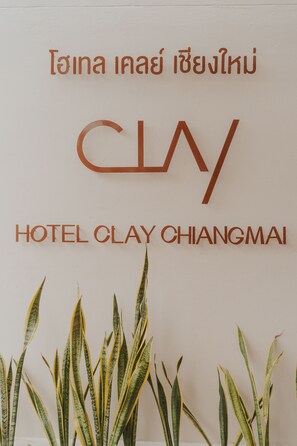 Een bord met Hotel Clay Chiangmai, met Thaise tekst boven de Engelse naam.
