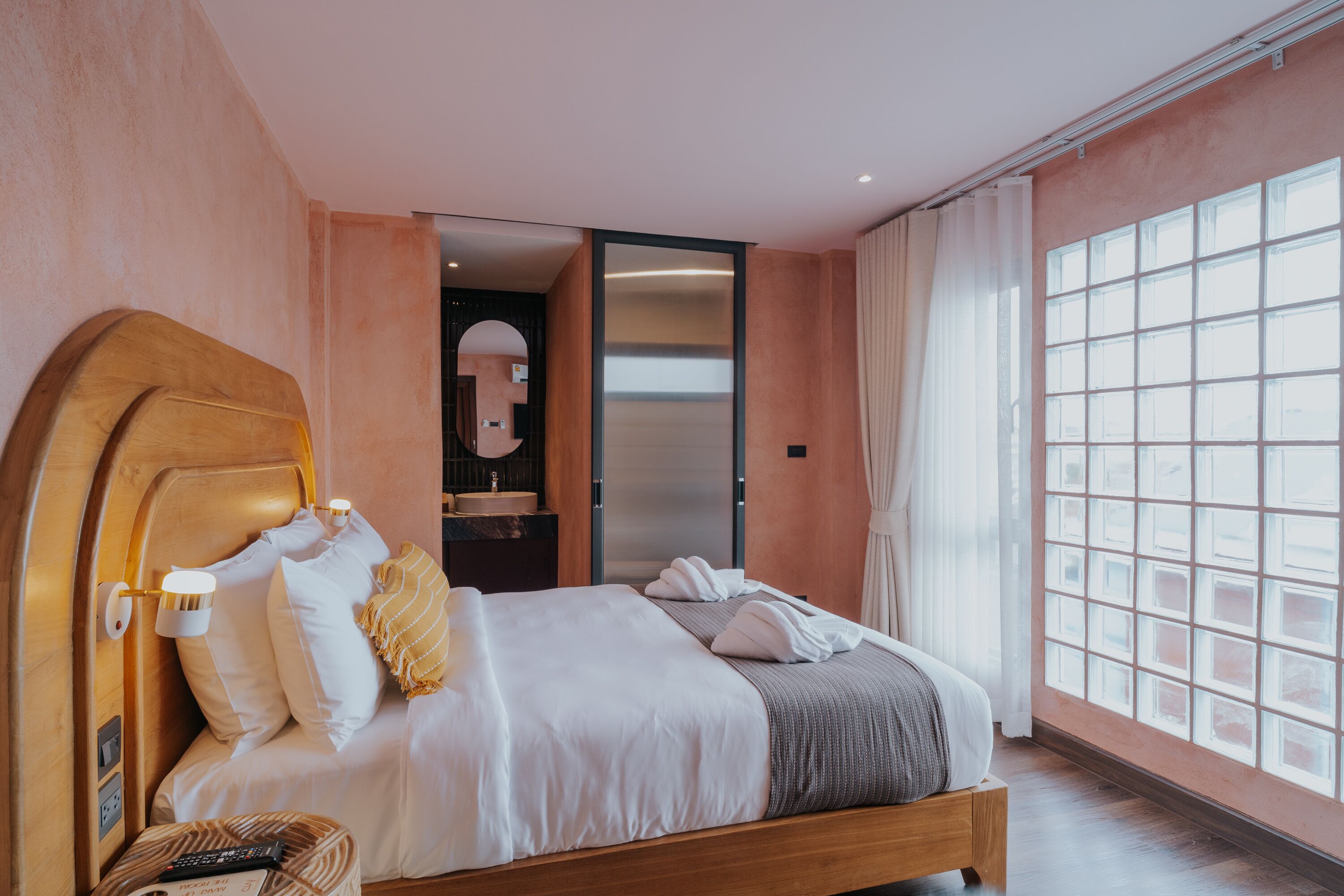 Une chambre moderne avec une tête de lit en bois, une grande fenêtre offrant une belle vue, une table de chevet avec une lampe et un miroir.