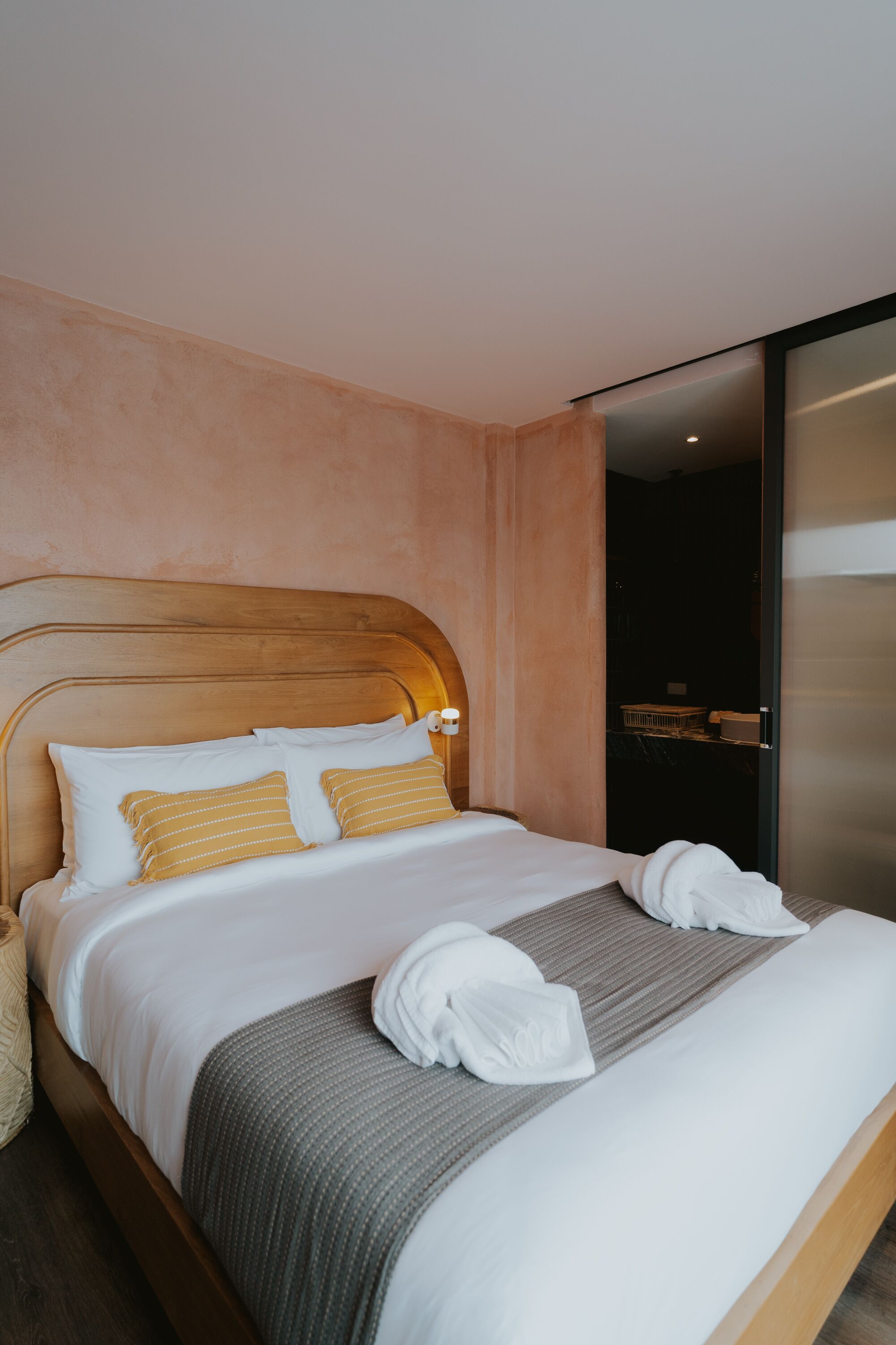 A neatly made bed with white and striped pillows, a grey blanket, and towels folded at the foot of the bed.