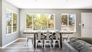 Uma área de refeições com mesa, cadeiras, janelas amplas e uma porta.