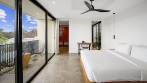 Habitación de hotel moderna con una cama grande, un balcón con sillas, una zona de comedor y vistas al exterior.