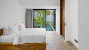 Un dormitorio con cama de madera, ropa de cama blanca, vista a una piscina y puerta corrediza de vidrio que da a un balcón.