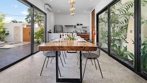 Un comedor moderno con una mesa de madera y sillas negras, ventanas amplias y plantas de interior.
