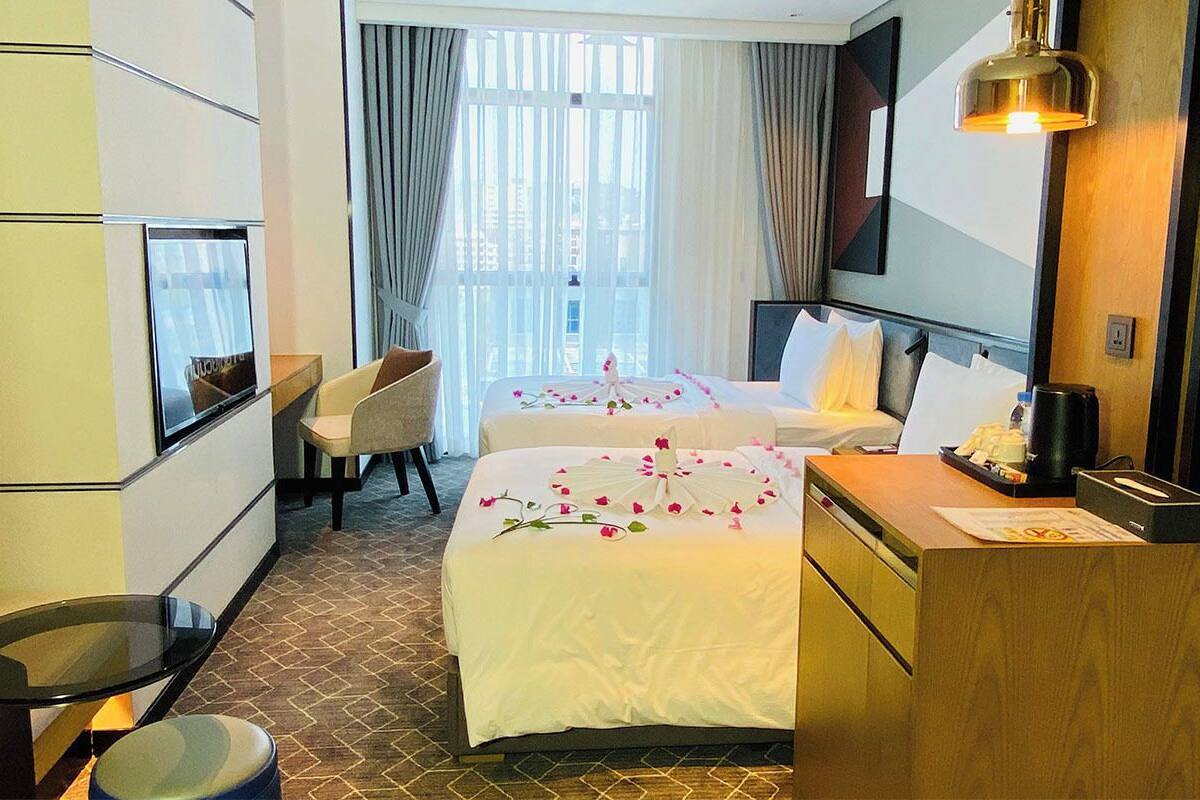 Una habitación de hotel con dos camas, un escritorio, una silla y un ventanal con cortinas.