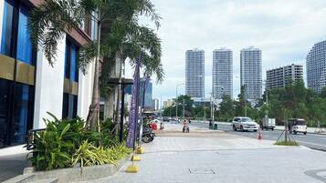 A modern urban street with tall buildings, a sidewalk lined with palm trees, and a few pedestrians.