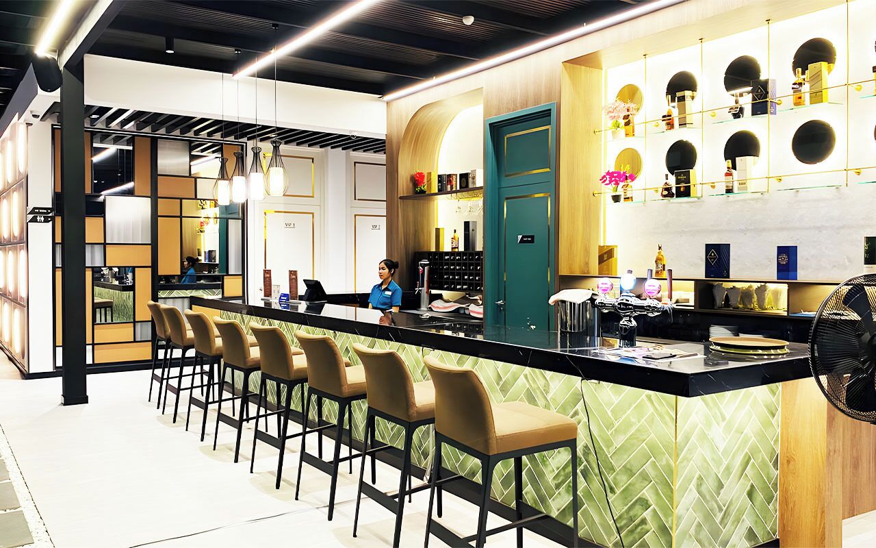 A modern bar area with a long counter, multiple bar stools, and a variety of bottles and glasses on shelves.