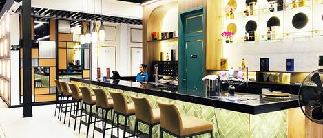 A modern bar area with a long counter, multiple bar stools, and a variety of bottles and glasses on shelves.