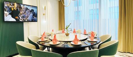 A dining room with a round table, green and white chairs, and a television mounted on the wall.