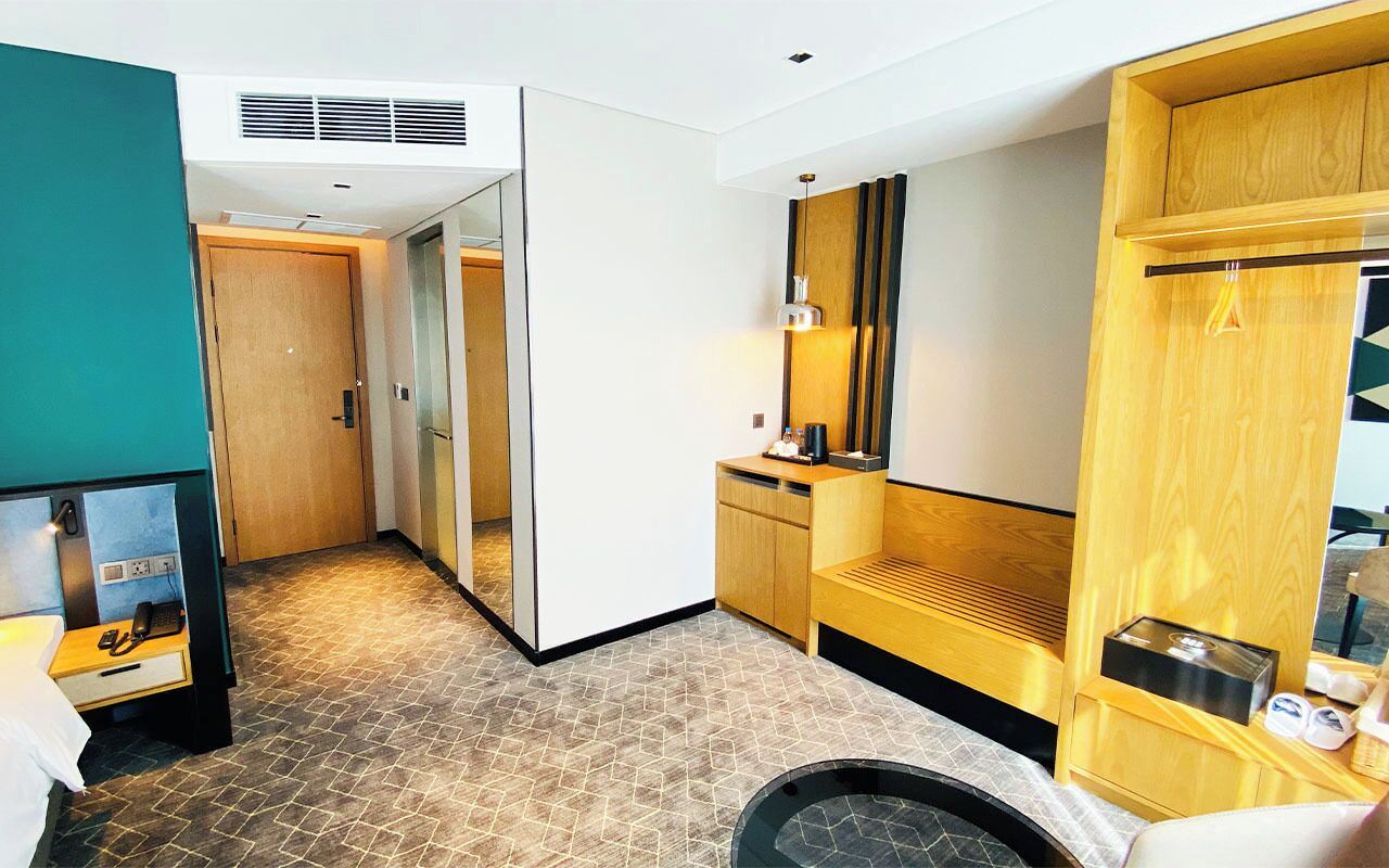 A hotel room with a mirrored wardrobe, a small seating area, and a compact bathroom.