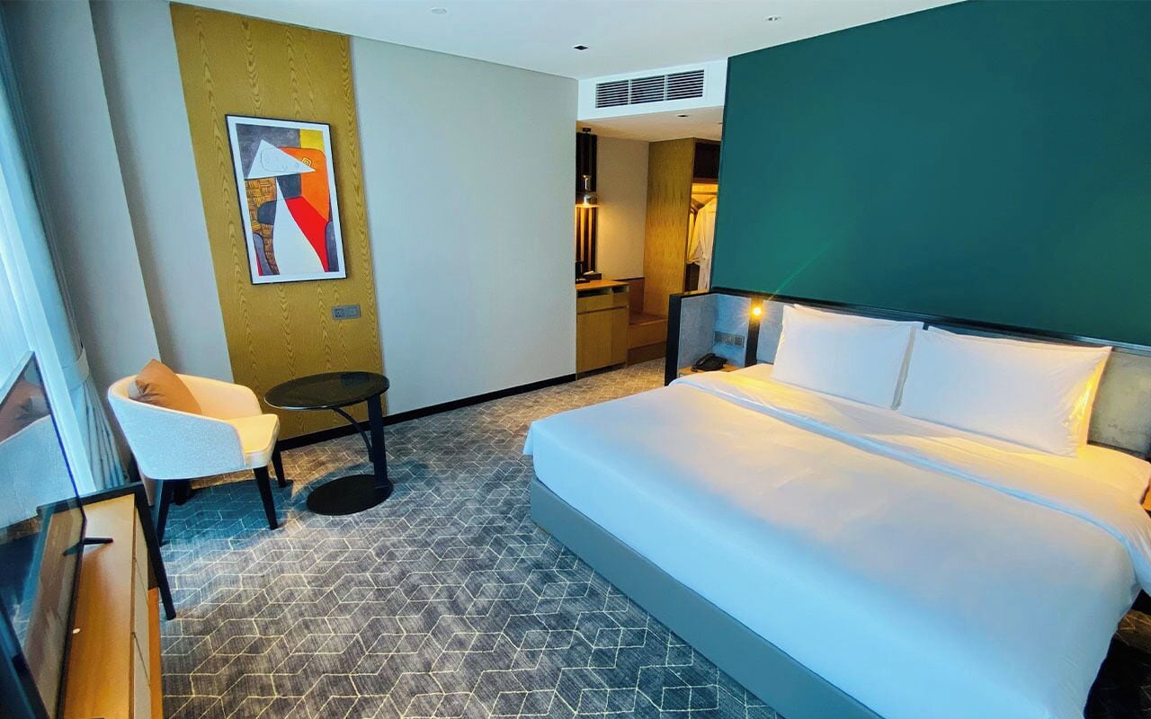 A hotel room with a large bed, a small desk, a chair, and a painting on the wall.