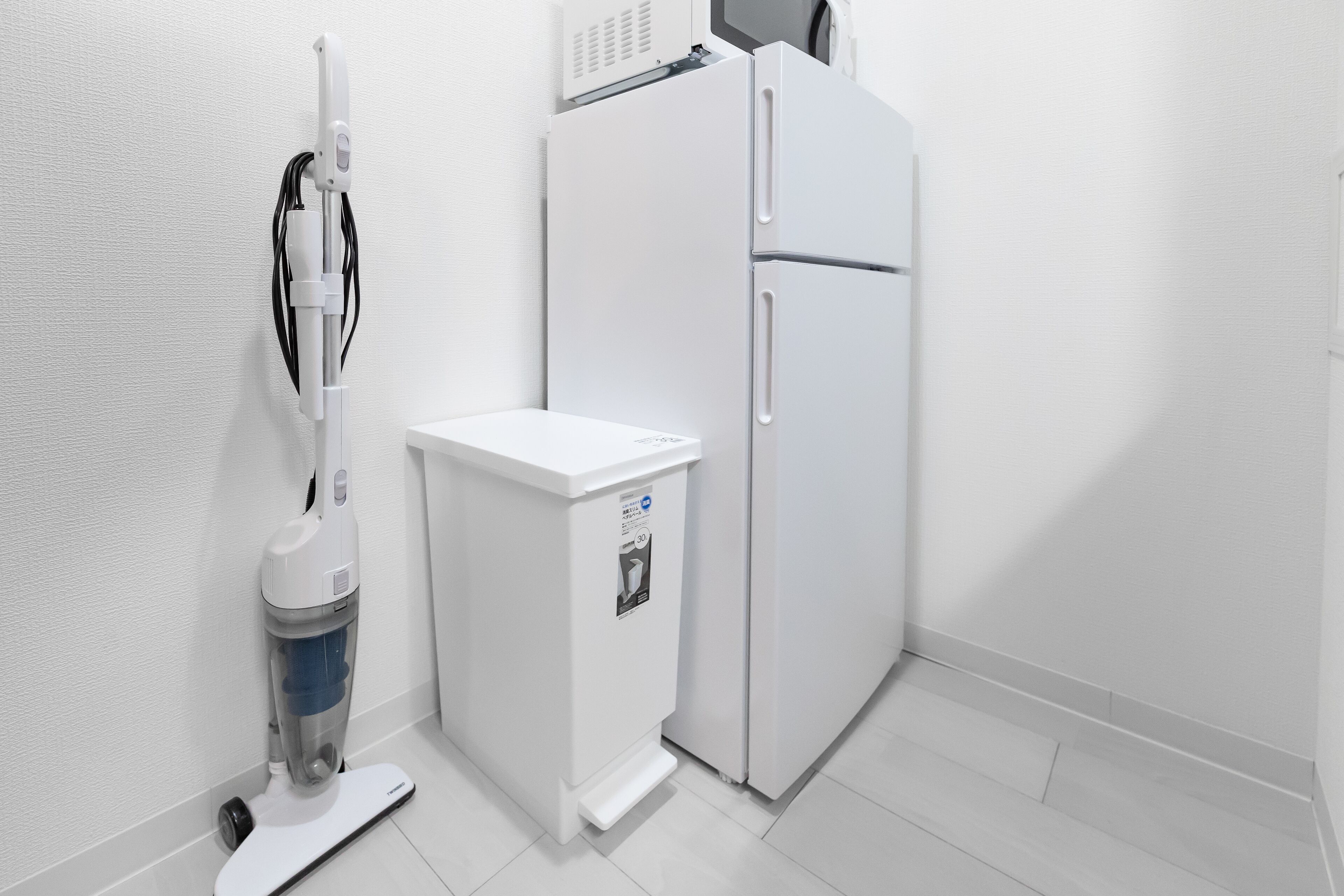 A clean, white bathroom with a toilet, a white cabinet, and a vacuum cleaner.