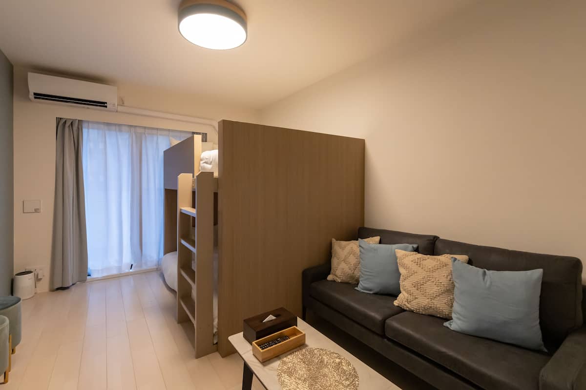 En moderne stue med en mørkebrun sofa, to lyseblå puder, et træskab og et lille bord med tissues og en fjernbetjening.